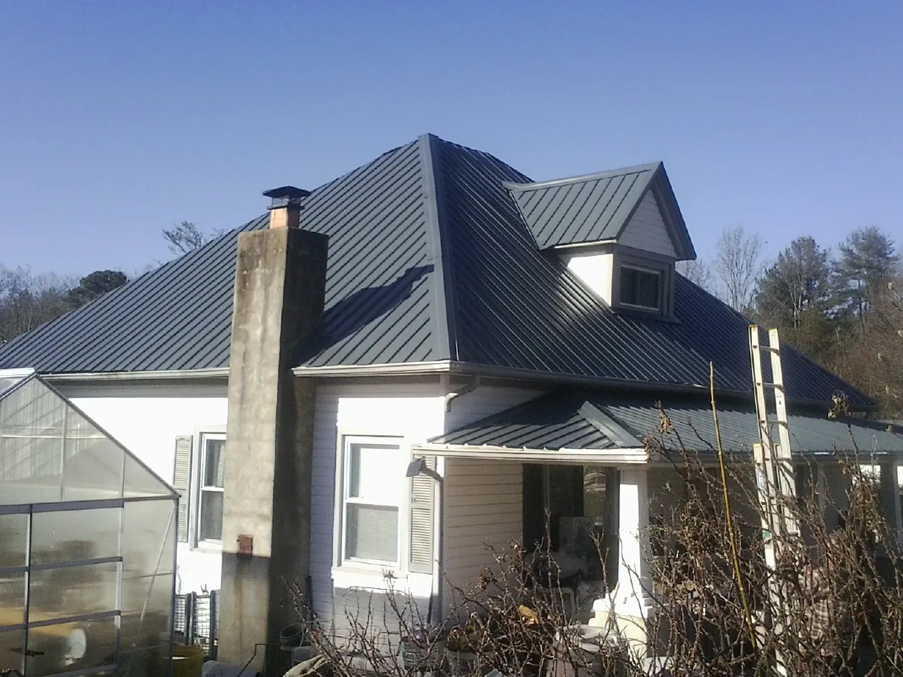 Dark blue standing seam metal roof on a white farmhouse with dormer — Slate & Tile Roof Repair by Roofing Brothers in Trinity