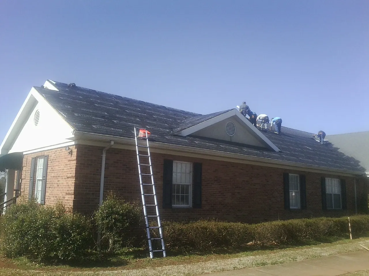 Crew tearing shingles off a brick ranch roof with a ladder set — Metal Roof Repair work by our crew in Trinity