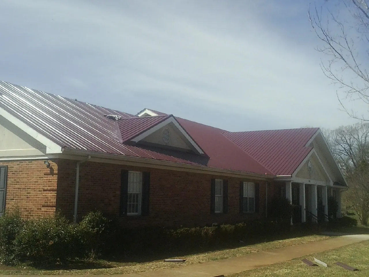 Red metal roof with gabled entries on a long brick building, from a Hail Damage Roof Repair job in Trinity