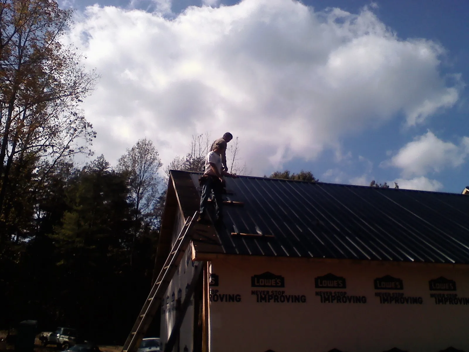 Roofer fastening dark metal panels high against a cloudy sky, from a Roof Inspection job in Trinity