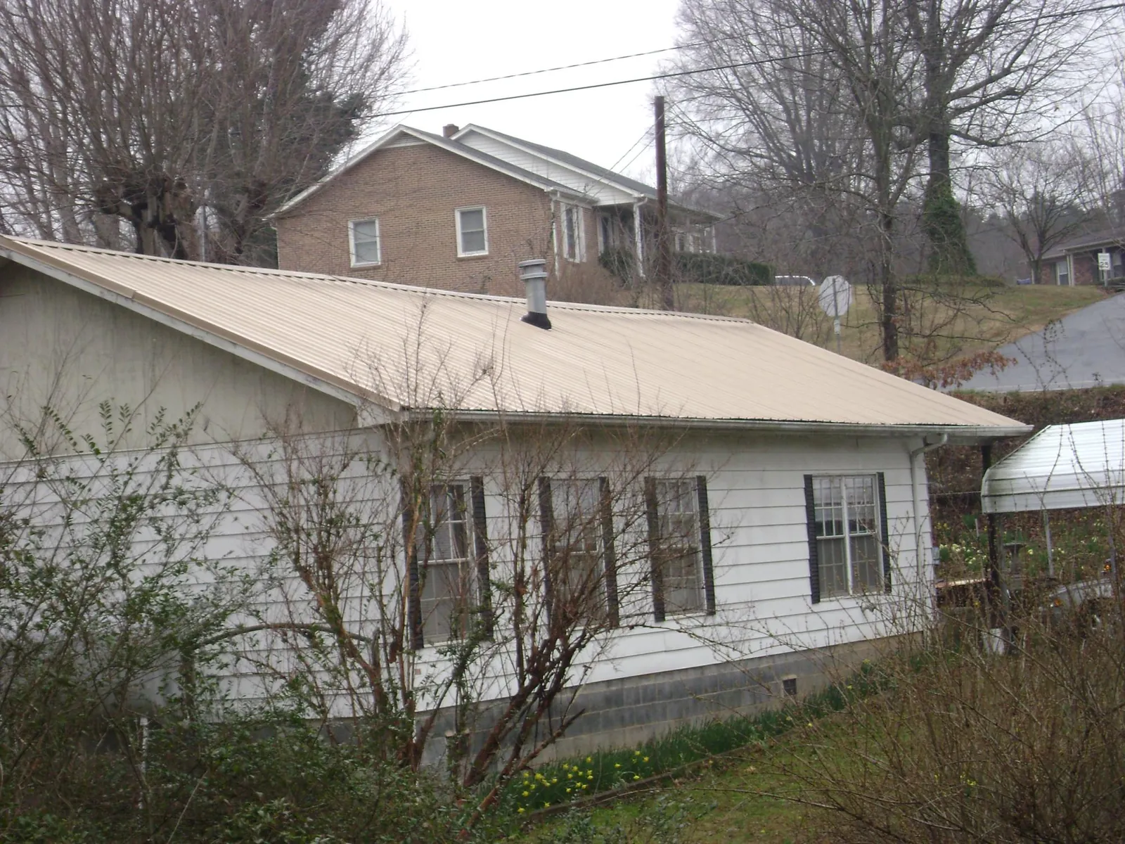 Tan metal roof on a white sided house set into a hillside — Commercial Roofing by Roofing Brothers in Trinity